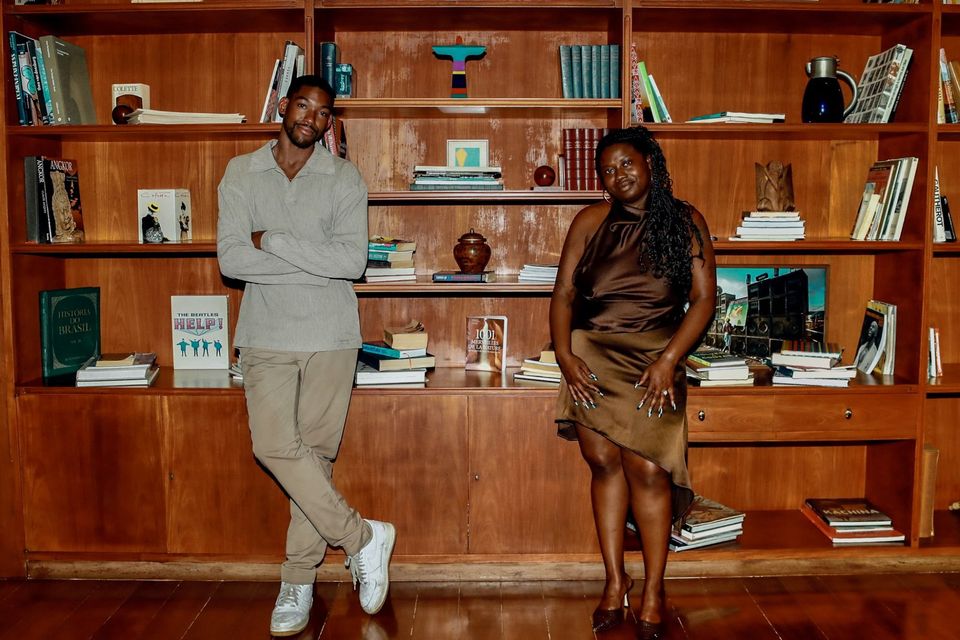 Joshua McKenzie German and Janel Moore standing in front of a wall of wooden bookshelves