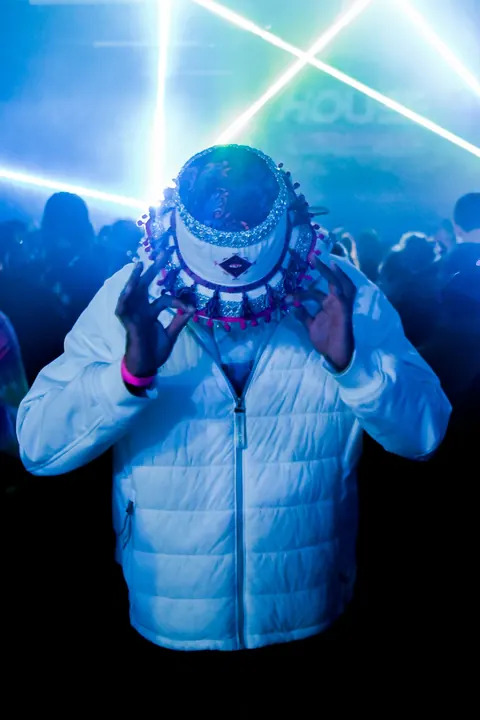 A performer in a quilted jacket stands beneath intense blue stage light.
