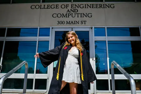 A graduate celebrates on the steps of an engineering building.