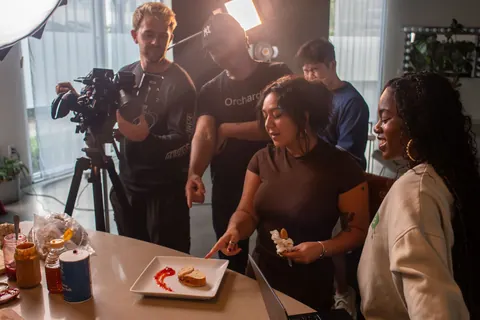 A small production crew gathers around a plated dish on a culinary set.