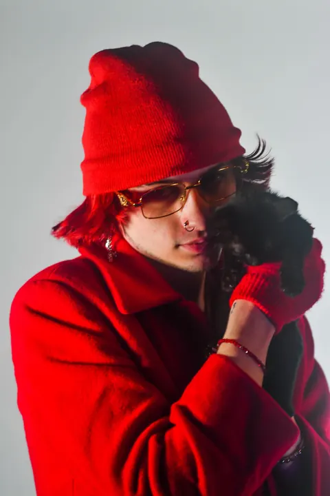 Fashion portrait of a model in a red coat and knit hat against a pale studio wall.