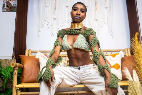 Fashion portrait of a model seated in a patterned green look and white trousers.