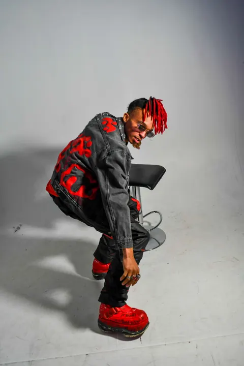 Fashion portrait of a man with red-tipped hair, red boots, and a painted black denim look.