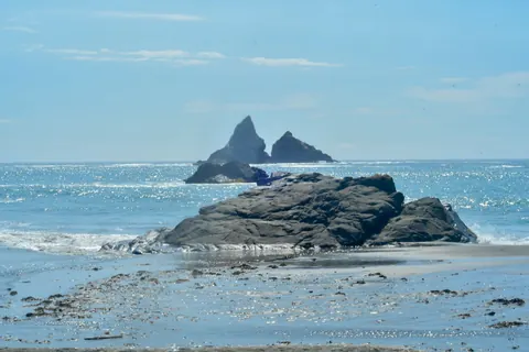 Two rock formations rise from bright blue water along the coast.