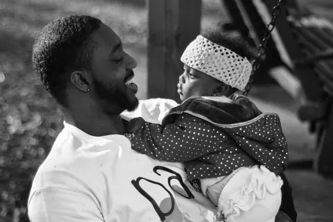 Black-and-white portrait of a father holding a baby outdoors.