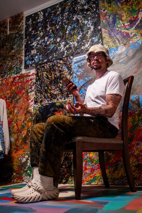Portrait of an artist seated in a colorful studio surrounded by his work.