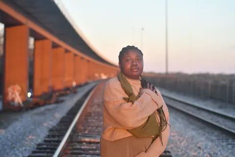 Portrait of a woman standing beside railway tracks in warm evening light.