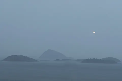 A full moon rises over fog-shrouded islands in Guanabara Bay, Rio de Janeiro.