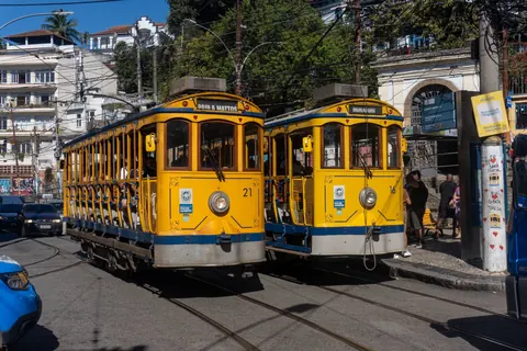 Two yellow trams meet on the tracks in Santa Teresa, Rio de Janeiro, passengers and pedestrians filling the street.