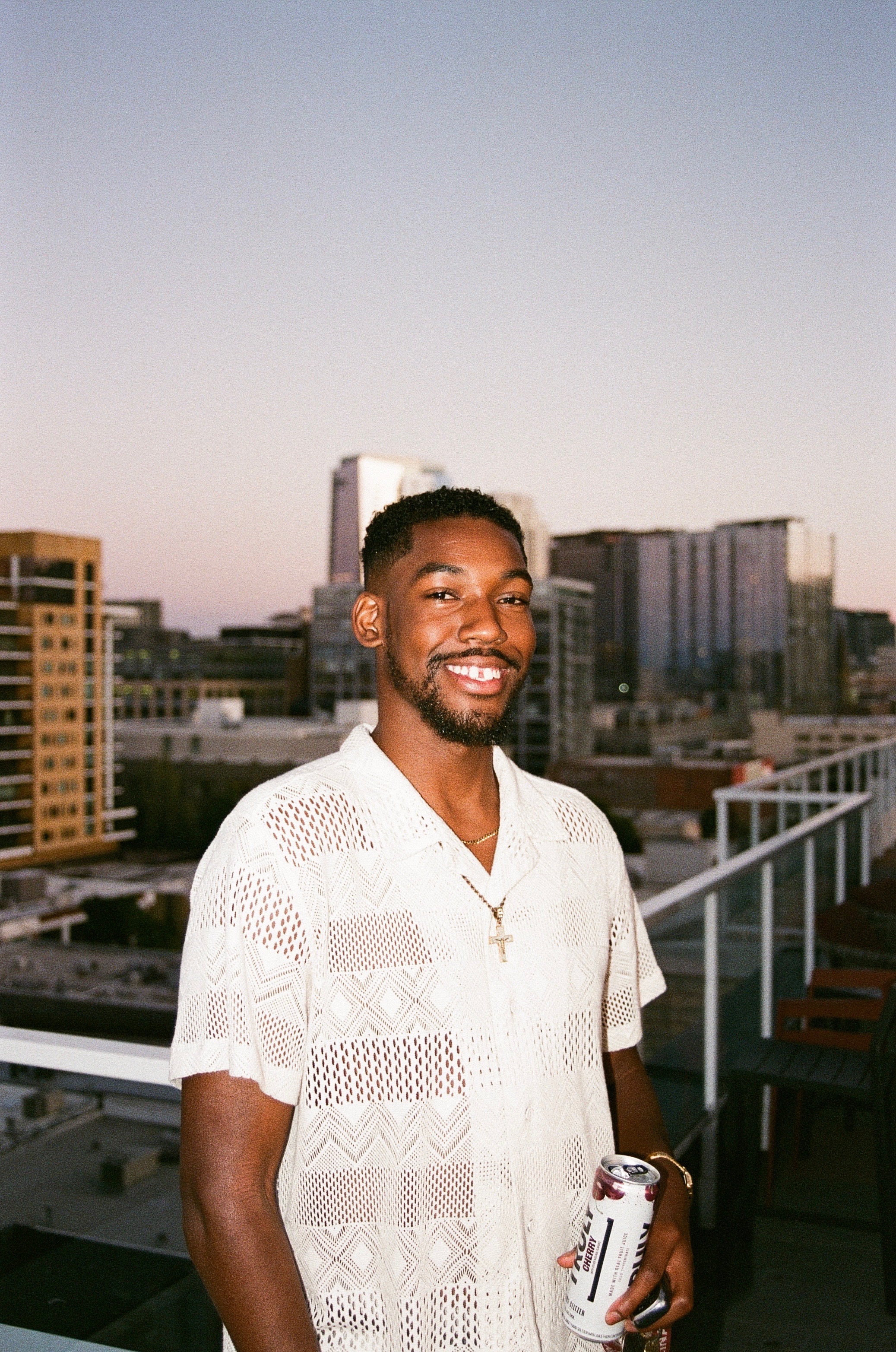 Joshua McKenzie German smiling on a rooftop above a city skyline at dusk