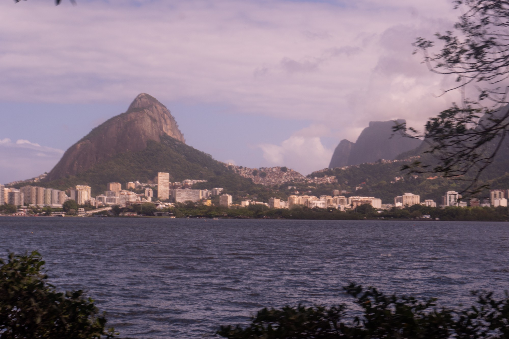 The peak of Dois Irmãos rises over a lagoon and the Rio de Janeiro skyline at dusk.